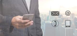 Un homme qui tient un smartphone dans sa main avec en arrière plan une ville style métropole américaine. En premier plan, sur la droite de l'homme sont placés 4 icônes: une enveloppe, un arobase, un ancien combinet de téléphone, comme dans les cabines téléléphoniques, et l'icône d'un smartphone