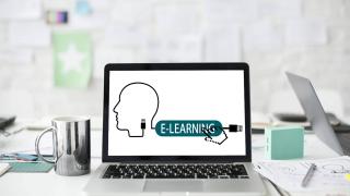 Sur un bureau un ordinateur portable est posé. Sur l&rsquo;écran de l&rsquo;ordinateur est le dessin d&rsquo;un cable. A l&rsquo;extrémité gauche le cable forme une tête, à droite il forme un embout USB et entre deux il y a une étiquette indiquant e-learning: apprentissage électronique