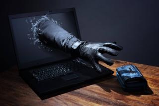 Main gantée qui s'introduit par l&rsquo;écran d&rsquo;un pc portable et vole le portefeuille posé sur le bureau