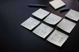 Un bureau sur lequel sont disposés des feuillets représentant les pages du sites sur lesquels le contenu est dessiné