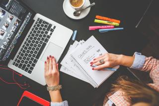 Expression des besoins sur bureau vue de dessus: mains de femmes écris sur carnet de notes devant un ordinateur portable